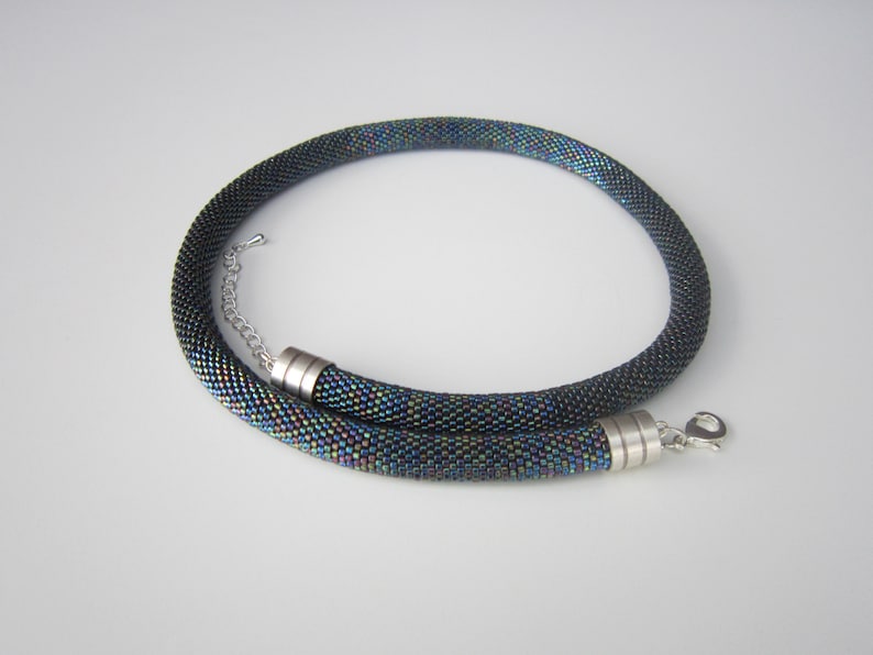 Op de afbeelding: Een zwarte kralenketting met iriserende kralen en zilveren magneetsluitingen.