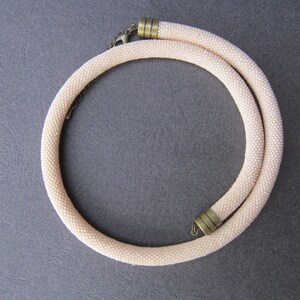 Op de afbeelding: Een delicate, cr&egrave;mekleurige kralenketting met twee goudkleurige sluitingen.