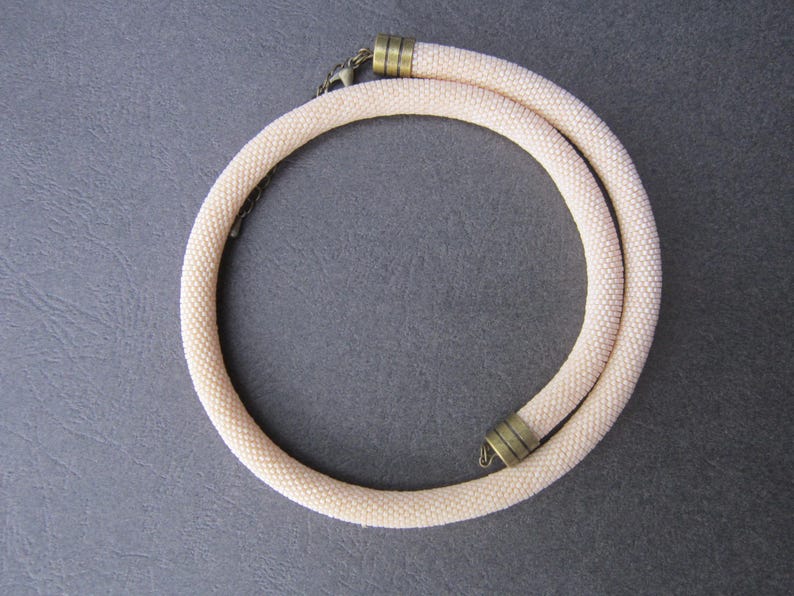 Op de afbeelding: Een delicate, cr&egrave;mekleurige kralenketting met twee goudkleurige sluitingen.