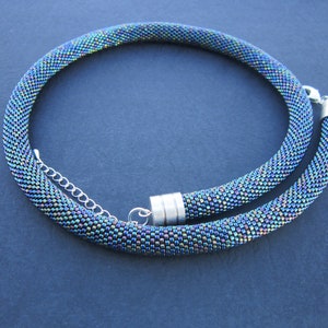 Op de afbeelding: Een kralenketting met een zilveren sluiting. De kralen zijn iriserend en hebben een blauwe, groene en paarse kleurstelling.