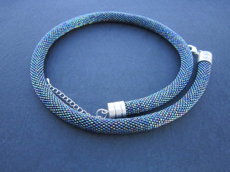 Op de afbeelding: Een kralenketting met een zilveren sluiting. De kralen zijn iriserend en hebben een blauwe, groene en paarse kleurstelling.