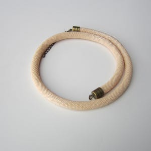 Op de afbeelding: Een delicate, cr&egrave;mekleurige kralenketting met een eenvoudig, minimalistisch ontwerp. De ketting is gemaakt van kleine, gelijkmatig verdeelde kralen en heeft een veilige sluiting.
