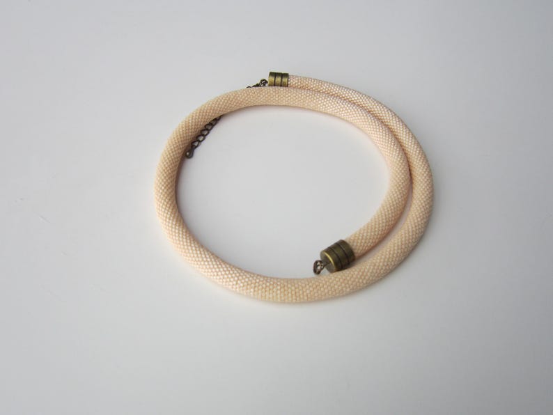 Op de afbeelding: Een delicate, cr&egrave;mekleurige kralenketting met een eenvoudig, minimalistisch ontwerp. De ketting is gemaakt van kleine, gelijkmatig verdeelde kralen en heeft een veilige sluiting.