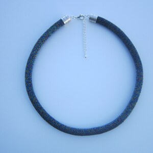 Op de afbeelding: Een donkerblauwe kralenketting met een zilveren sluiting. De kralen zijn klein en iriserend, waardoor een glinsterend effect ontstaat.