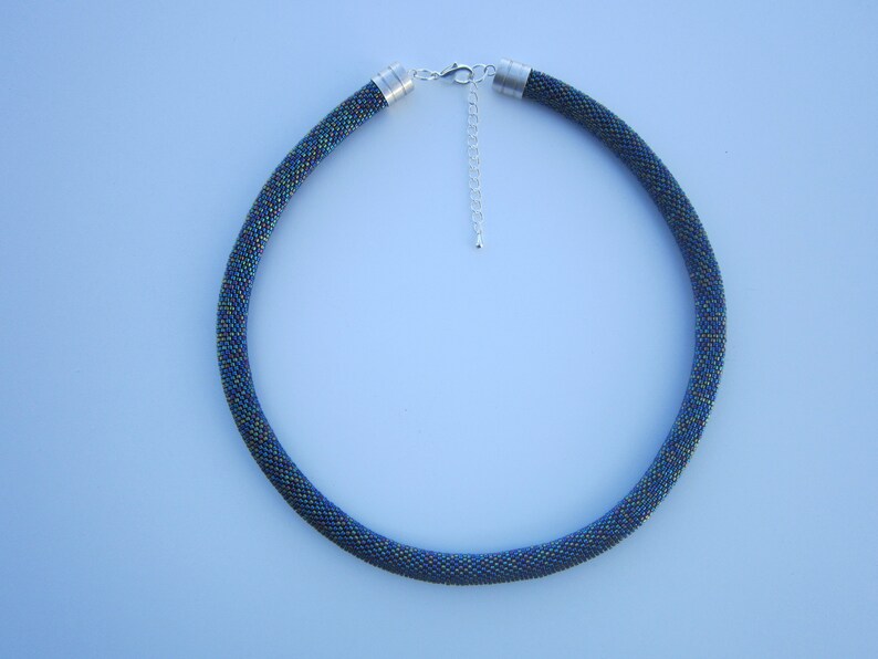 Op de afbeelding: Een donkerblauwe kralenketting met een zilveren sluiting. De kralen zijn klein en iriserend, waardoor een glinsterend effect ontstaat.