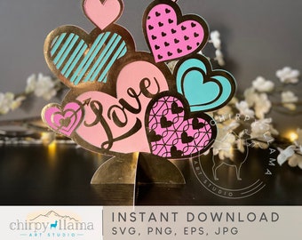 May include: A pink and blue layered heart-shaped papercraft with the word "Love" in gold lettering. The hearts are decorated with stripes, polka dots, and swirls.