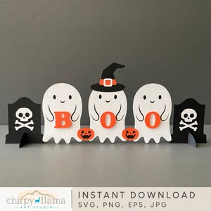 May include: A Halloween-themed decoration featuring three white ghost figures spelling "BOO" with orange letters. The center ghost wears a witch hat. Two black tombstones with skull and crossbones flank the ghosts. Small orange jack-o'-lanterns are also present.