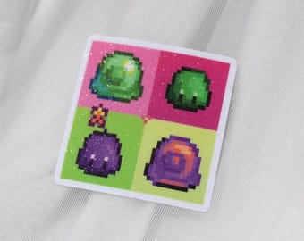 May include: Square sticker with a pixelated design featuring four different colourful, cartoonish slime creatures. The sticker has a glittery border and is divided into pink and green quadrants. The slimes are green, purple, and orange.