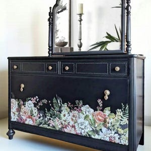 May include: Black dresser with a floral design on the front. The dresser has a matching mirror, gold-colored drawer pulls, and decorative trim. The mirror has an arched top and is flanked by decorative posts.