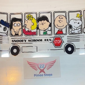 May include: A yellow school bus with the words "Snoopy School Bus" and a red "Stop" sign. The bus is filled with cartoon characters from the Peanuts comic strip, including Snoopy, Charlie Brown, Lucy, and Linus.