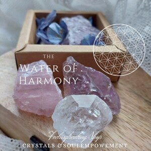 Könnte beinhalten: Eine Holzkiste gefüllt mit blauen Trockenblumen und Kristallen. Drei rohe Kristalle befinden sich vor der Kiste: ein rosa Rosenquarz, ein klarer Quarz und ein Amethyst. Der Text lautet "THE WATER OF HARMONY".