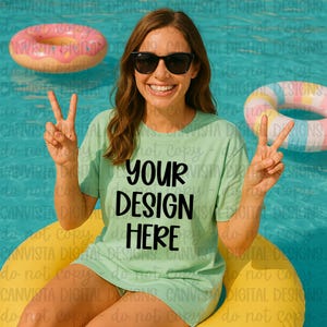 Könnte beinhalten: Eine Frau trägt ein hellgrünes T-Shirt mit dem schwarzen Text "YOUR DESIGN HERE". Sie trägt eine Sonnenbrille und zeigt mit ihren Fingern ein Friedenszeichen. Im Hintergrund befinden sich aufblasbare Poolspielzeuge in einem Pool.