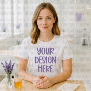 May include: A woman wearing a white t-shirt with the text "YOUR DESIGN HERE" in purple. The image includes a small vase of lavender, a jar of honey, and a folded white cloth on a wooden table.