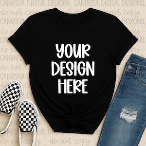 May include: Black t-shirt with the text "YOUR DESIGN HERE" in white. The shirt is styled with a knot at the waist and paired with blue jeans and checkered slip-on shoes.