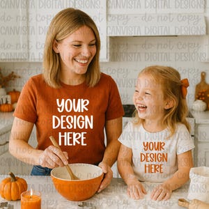 May include: Two short-sleeved t-shirts, one rust-colored and one white, both with the text "YOUR DESIGN HERE" in a contrasting color. The shirts are worn by a woman and a child. The image suggests a family-themed product.