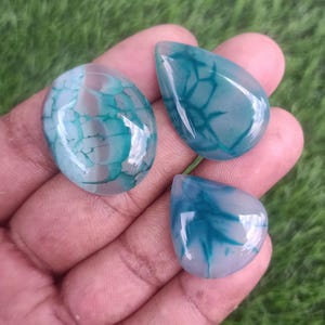 Puede incluir: Tres cabujones de ágata verde y blanca con un patrón de remolino. Los cabujones tienen forma de lágrima y tienen una apariencia translúcida.