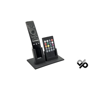 Könnte beinhalten: Ein schwarzer Fernbedienungsständer mit zwei Steckplätzen für Fernbedienungen. Der Ständer ist aus Kunststoff und hat ein elegantes, modernes Design. Der Ständer ist perfekt zum Organisieren und Aufbewahren von Fernbedienungen.