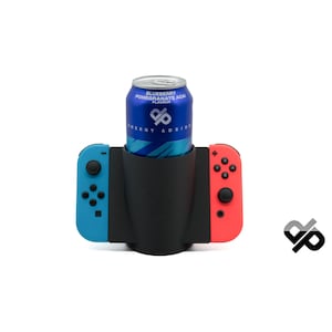 Könnte beinhalten: Ein schwarzer Silikon-Becherhalter für einen Nintendo Switch-Controller mit einem blauen und roten Controller auf jeder Seite. Eine Dose mit einem Energy-Drink aus Blaubeere, Granatapfel und Açai befindet sich im Halter.
