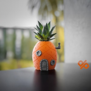 Könnte beinhalten: Ein 3D-gedruckter Ananas-Pflanztopf mit einer grauen Tür und Bullaugendetails. Eine kleine Sukkulente wächst im Topf.