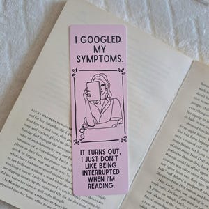 May include: A pink bookmark with the text "I Googled My Symptoms" and "It turns out, I just don't like being interrupted when I'm reading." A black and white illustration of a person reading is also on the bookmark.