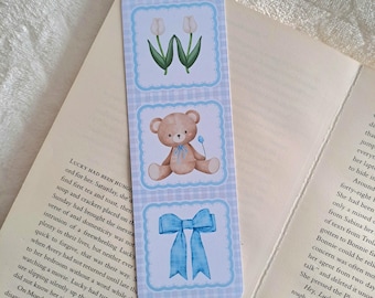 May include: A blue and white bookmark with three sections. The top section features two white tulips on a blue and white checked background. The middle section features a brown teddy bear with a blue bow tie on a blue and white checked background. The bottom section features a blue bow on a blue and white checked background.