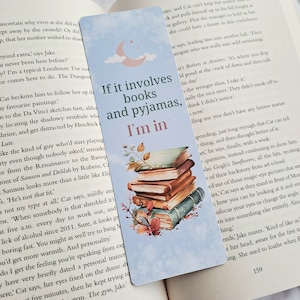 May include: A blue and white bookmark featuring a stack of books and a crescent moon illustration. The text on the bookmark reads "If it involves books and pyjamas, I'm in."
