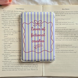 May include: A clear phone case with a purple and white striped pattern. The case displays the text "Lover of fictional crushes" within a decorative frame, and a small "Perfect Match" graphic.