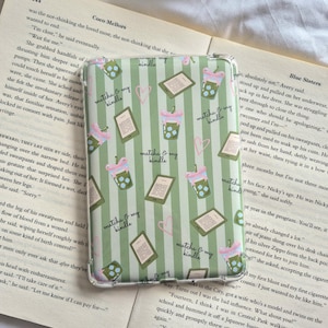 May include: A clear protective e-reader case featuring a repeating pattern of green vertical stripes, illustrations of iced matcha drinks, e-readers, and pink hearts. The text "matcha & my kindle" is printed in a cursive script throughout the design.