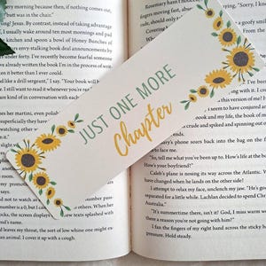 May include: A bookmark featuring the text "JUST ONE MORE Chapter" in green and yellow, adorned with yellow sunflowers and green leaves. The bookmark is positioned within an open book.