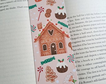 May include: A pink bookmark featuring a gingerbread house, Christmas trees, candy canes, and cookies. The bookmark has a white border and the number 19 printed in the top right corner.