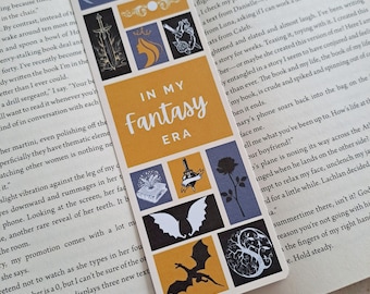 May include: A bookmark with a yellow and orange background featuring a dragon, a sword, a crown, a rose, and a book. The bookmark has the text "In My Fantasy Era" in black lettering.