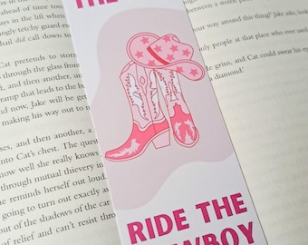 May include: Pink bookmark with a pink cowboy boot and hat illustration. The bookmark has the text "Wear the Hat" and "Ride the Cowboy" in pink.
