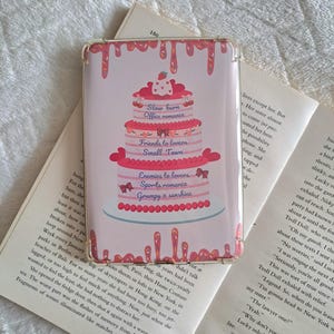 May include: A pink and white cake with four tiers. Each tier has a different design and text. The top tier says "Slow burn Office romance". The second tier says "Friends to lovers Small Town". The third tier says "Enemies to lovers Sports romance". The bottom tier says "Grumpy x sunshine".