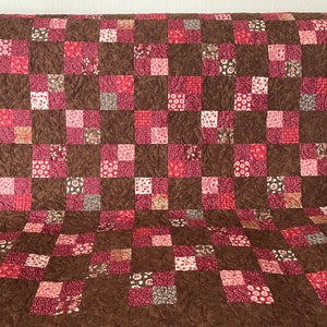 May include: A brown and red patchwork quilt with a quilted pattern. The quilt is made up of squares of different fabrics, some with floral patterns and some with solid colors.