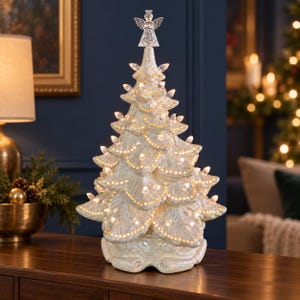 May include: A pearlescent white ceramic tabletop Christmas tree featuring scalloped branches, numerous small integrated warm white LED lights, and a clear glass angel topper. The surface has a glossy, iridescent finish that reflects light.