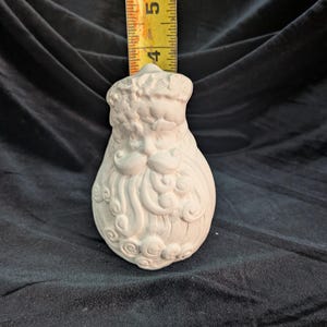 May include: A white ceramic Santa Claus figurine, unpainted, with detailed facial features and a long beard. The figurine is approximately 4.5 inches tall, as measured by a yellow measuring tape. The Santa Claus figurine is a decorative item.