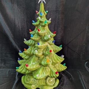 May include: A ceramic Christmas tree in a vibrant green hue, adorned with colorful lights and a star topper. The tree features a classic design with detailed textures and a glossy finish, perfect for holiday decor.