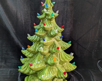 May include: A green ceramic Christmas tree with a star on top, decorated with multi-coloured lights. The tree has a glossy finish and a traditional design, ideal for festive home decoration.