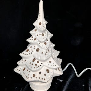 May include: A white ceramic Christmas tree with a textured surface and numerous circular cutouts. The tree has a tiered design and sits on a small, round base. A white electrical cord extends from the base.