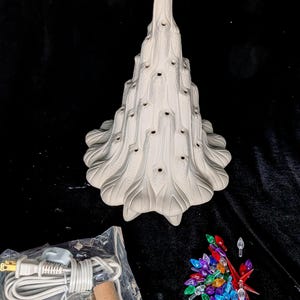 May include: A matte white ceramic Christmas tree figurine with a textured surface and numerous small holes for light bulbs. Included are a white electrical cord with a switch and a collection of assorted colorful plastic light bulb inserts.