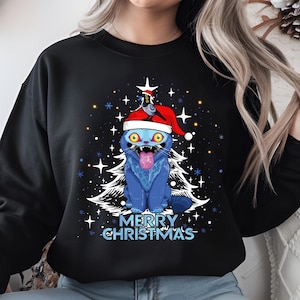 May include: Black sweatshirt featuring a blue cat wearing a Santa hat, with a white Christmas tree and the text "MERRY CHRISTMAS." The cat has yellow eyes and its tongue is sticking out. White stars and snowflakes are scattered around the design.