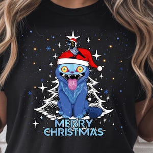 May include: Black t-shirt featuring a blue cat with yellow eyes, wearing a Santa hat, and sticking out its tongue. A white Christmas tree and the words "MERRY CHRISTMAS" are below the cat, with a starry background.