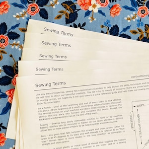 Könnte beinhalten: Nahaufnahme eines weißen Blattes Papier mit dem Titel "Sewing Terms" in schwarzer Schrift. Das Papier ist in der Mitte gefaltet und enthält mehrere Zeilen Text, die verschiedene Nähbegriffe erklären, darunter "Back Stitch", "Basting" und "Bias".