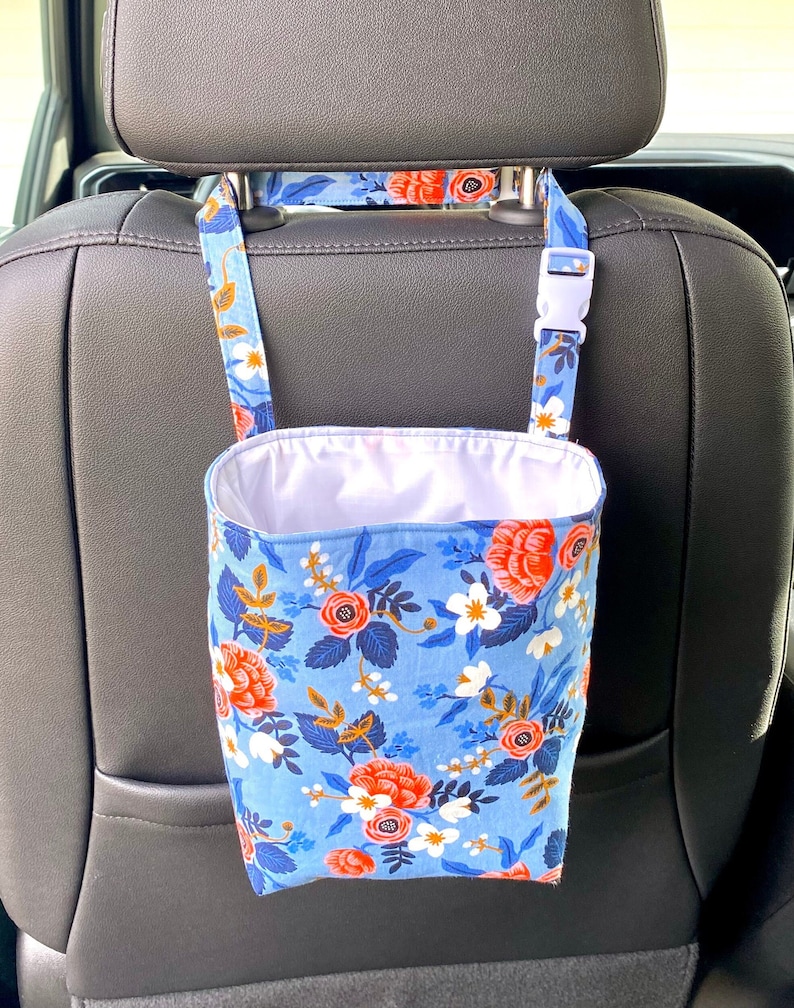 Flowered fabric bag for litter or storage bag hanging by a strap on back of black car seat. White buckle on strap. Inside of bag is white,  outside is in blues, white and pinks. Rifle Paper Co floral fabric. Instant download digital sewing pattern