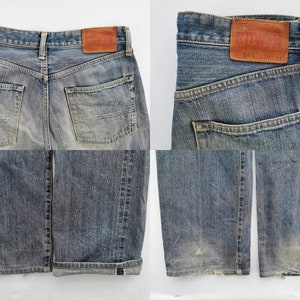 May include: Faded blue denim jeans with a classic five-pocket design. The jeans feature a leather patch with the brand name and size details. The cuffs are rolled up, revealing a contrasting fabric. The jeans have a worn look.