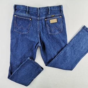 Puede incluir: Vaqueros de mezclilla azul oscuro con un dise&ntilde;o cl&aacute;sico de cinco bolsillos. Presentan el logotipo de Wrangler en el bolsillo trasero y un parche de cuero. Los vaqueros tienen un corte de pierna recta y est&aacute;n hechos de un material de mezclilla duradero.