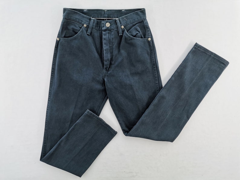 K&ouml;nnte beinhalten: Dunkelblaue Jeans mit klassischem F&uuml;nf-Taschen-Design. Die Jeans hat einen Knopf- und Rei&szlig;verschluss sowie silberne Nieten. Die Hose liegt flach auf einer wei&szlig;en Oberfl&auml;che.