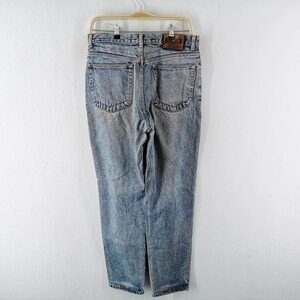 Op de afbeelding: Lichtblauwe denim jeans met een vervaagde wassing, hangend aan een houten hanger. De jeans hebben een klassiek ontwerp met vijf zakken, een leren patch en een rechte pijp. De achterzakken hebben een decoratieve steek.