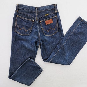Op de afbeelding: Donkerblauwe denim jeans met een klassiek vijf-zakken ontwerp. Voorzien van een bruine leren patch en het Wrangler-logo. De achterzakken hebben de kenmerkende Wrangler-stiksels.