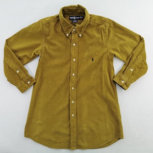 Puede incluir: Camisa de pana amarillo mostaza con botones y mangas largas. Cuenta con cuello abotonado, puños abotonados y un pequeño logotipo bordado en el pecho. Un estilo de camisa clásico.